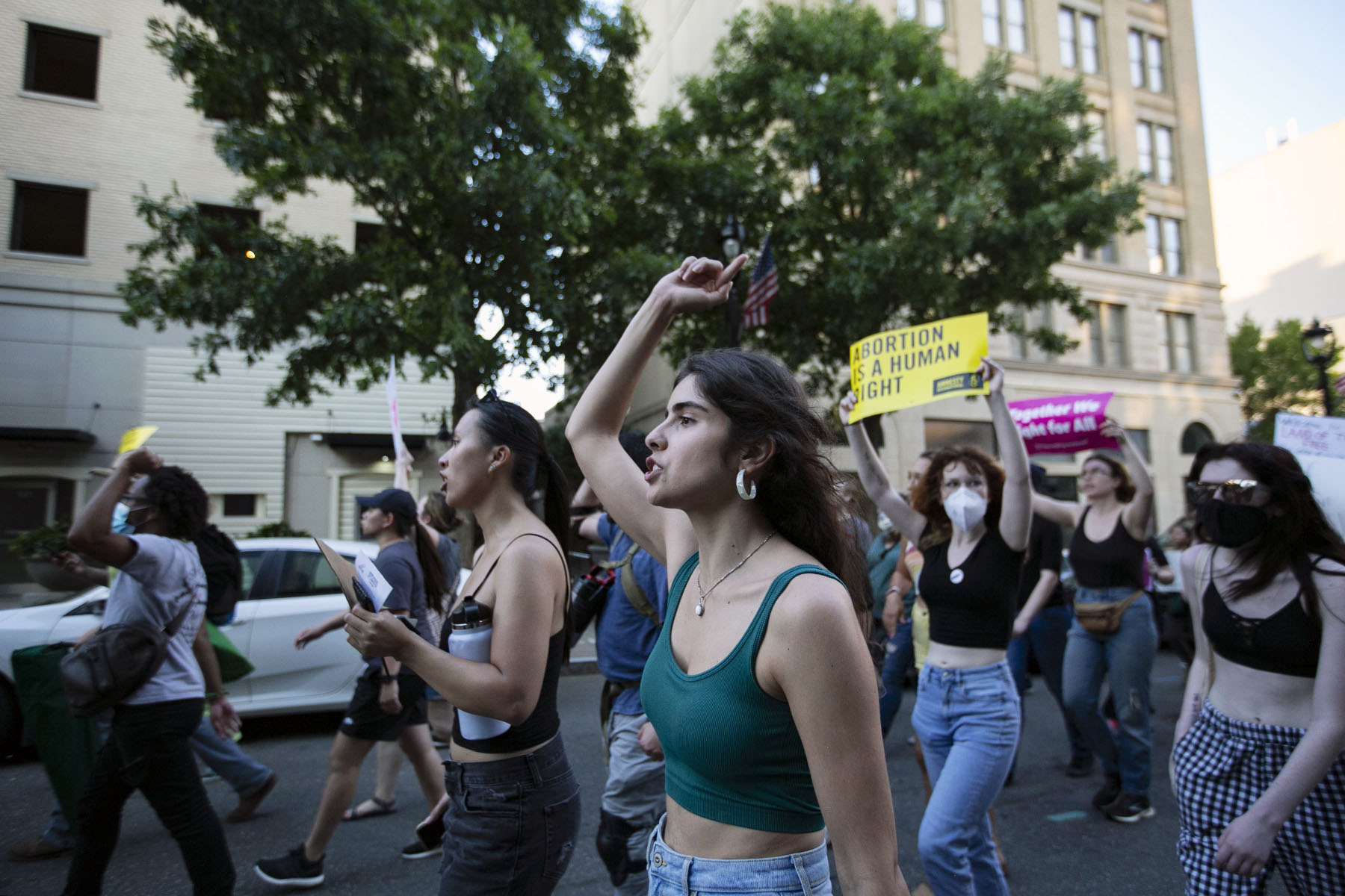 A group of protestors marches on a city street, raising signs and fists in the air.