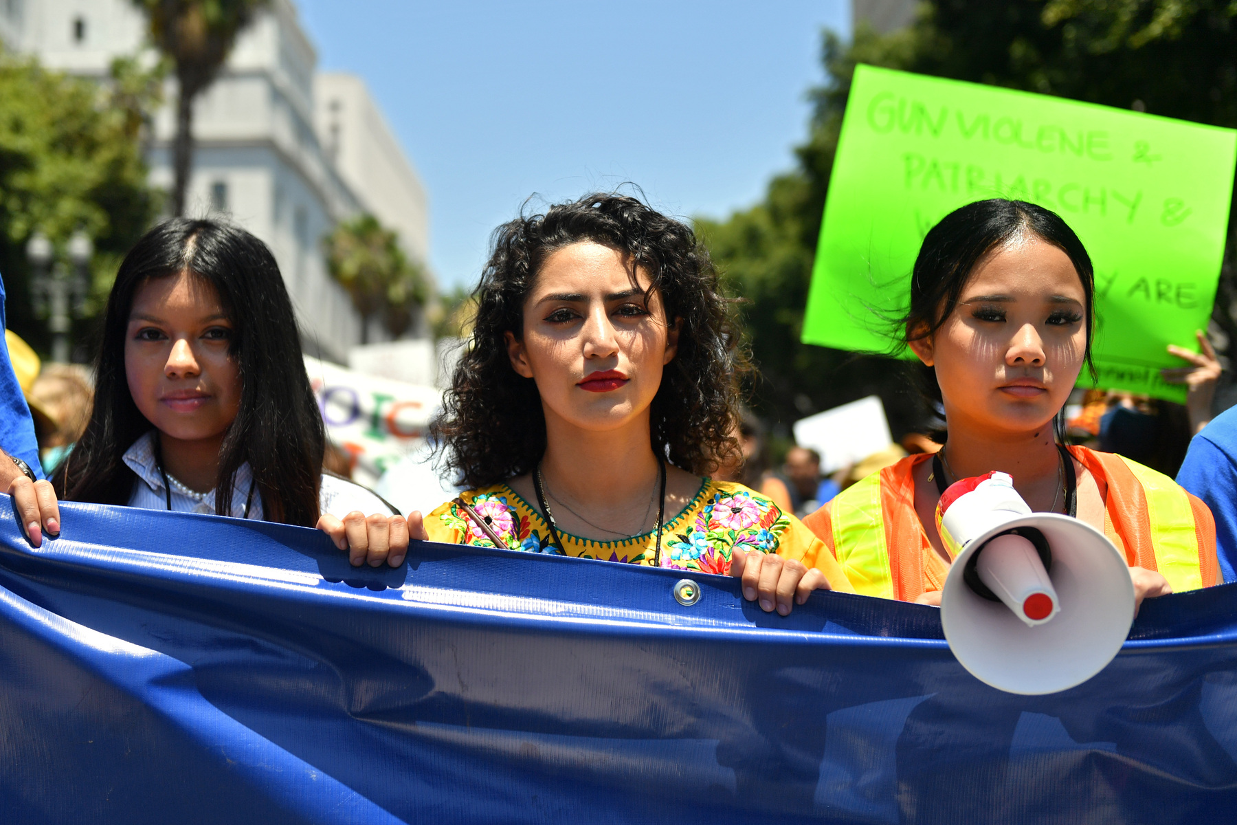 Three protestors carry a large blue banner and a megaphone while participating in a March For Our Lives protest.