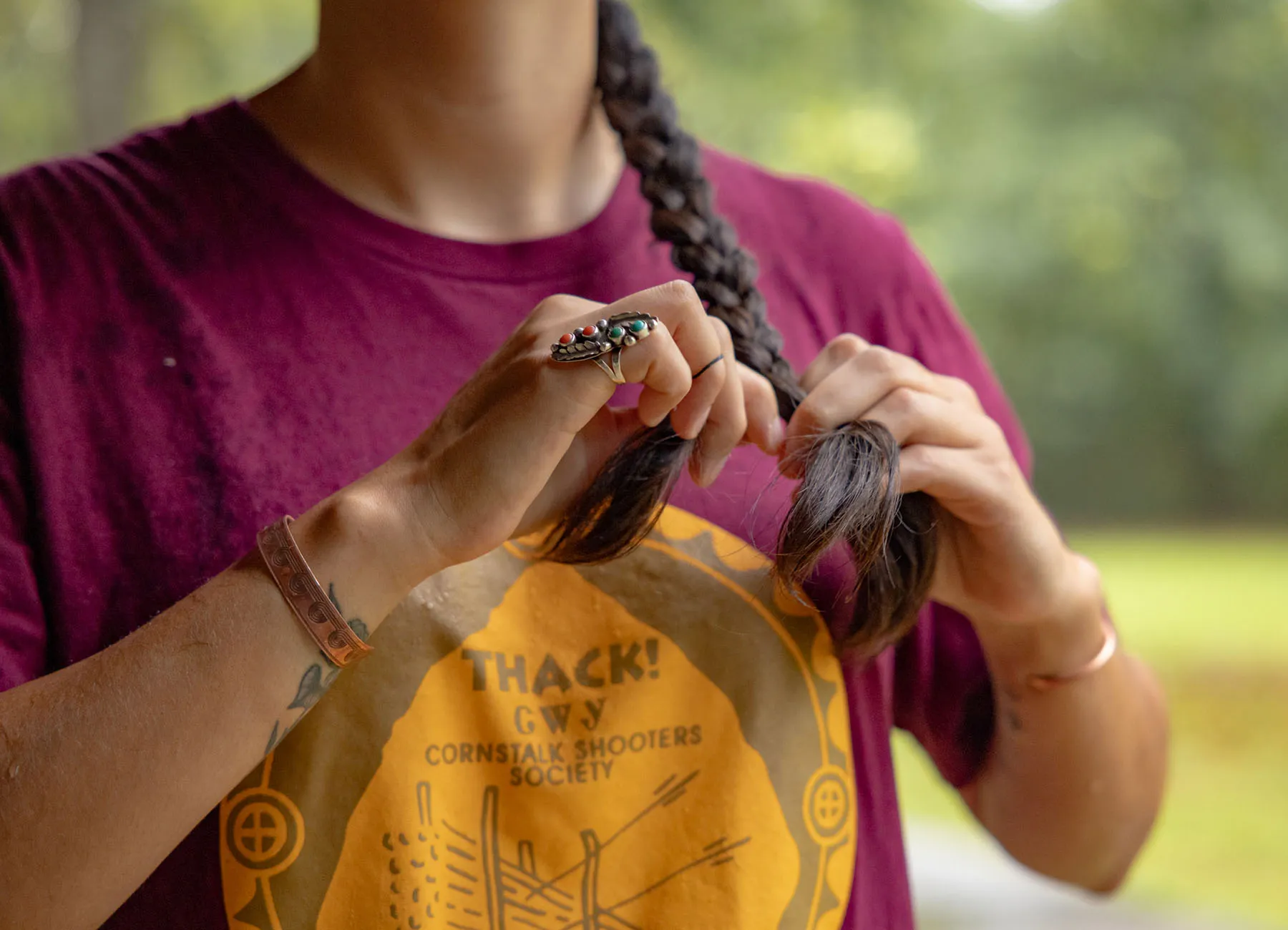 Detail of a native woman seen braiding her hair. Her face is not shown.