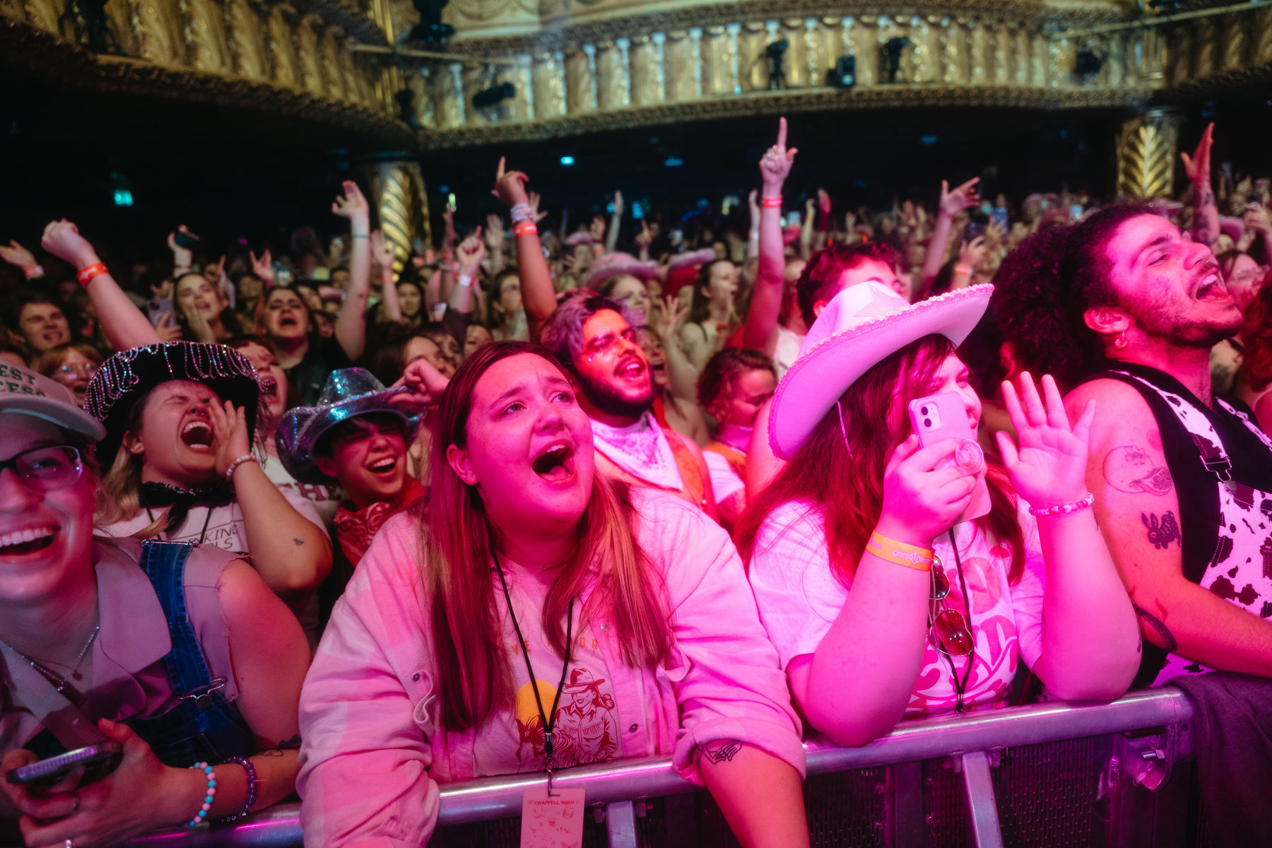 Concert attendees scream and sing while pressed against the stage barrier in an indoor theater.