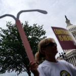 A woman holds up a sign and a replica of a intrauterine device outside the Capitol.