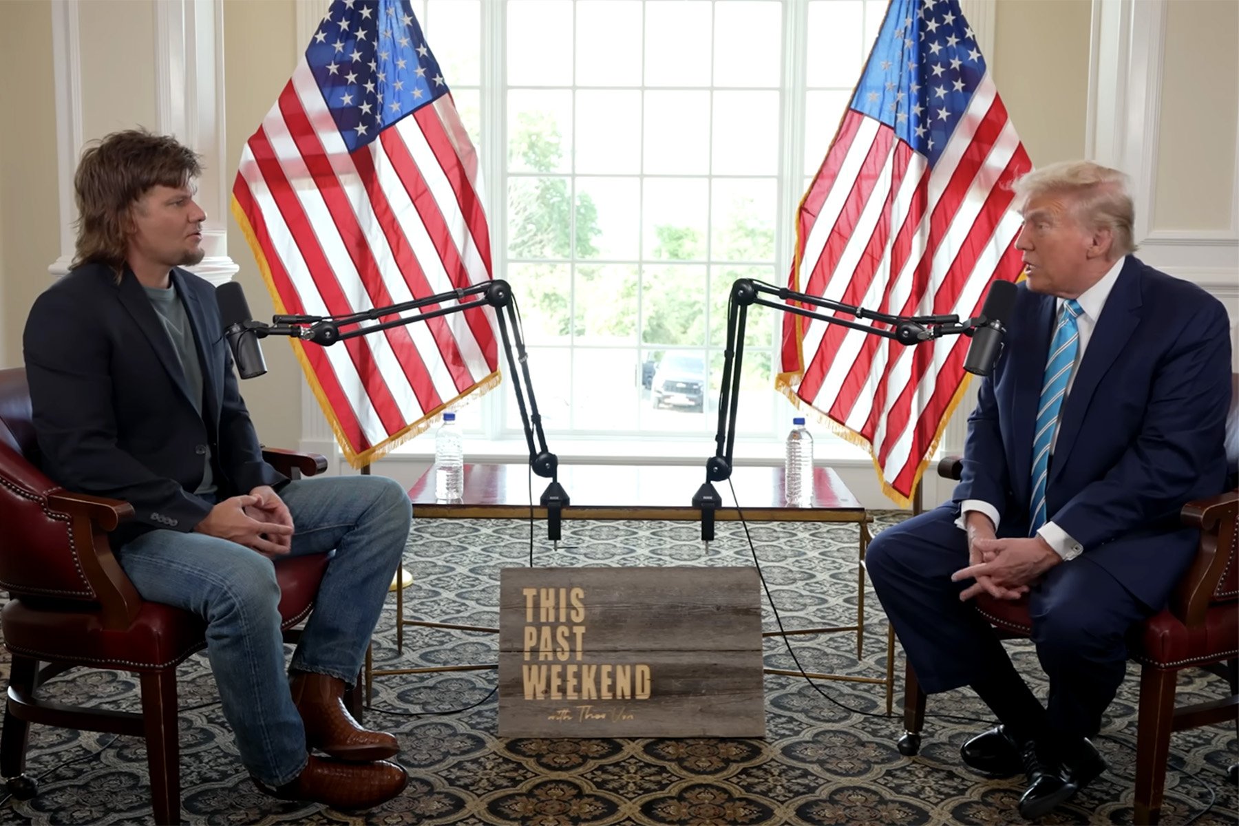 El expresidente Donald Trump y el comediante Theo Von durante una entrevista en "Este pasado fin de semana," con ambos hombres sentados en una sala adornada con dos banderas estadounidenses y micrófonos.