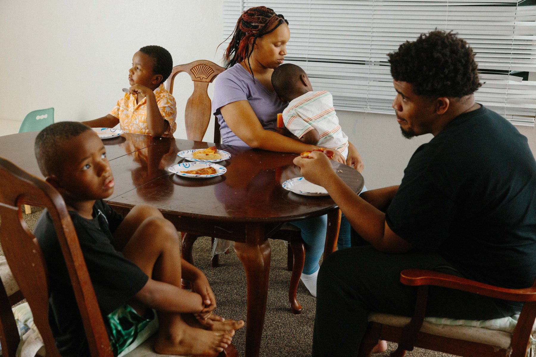 A mother and four of her sons sit at the dinner table, all facing and looking in different directions.