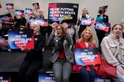 A group of women cheer as they hold signs saying 