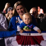 A woman holds a baby in a crowd.