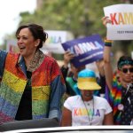 Kamala Harris waves to a crowd while in a car that is part of a Pride parade.