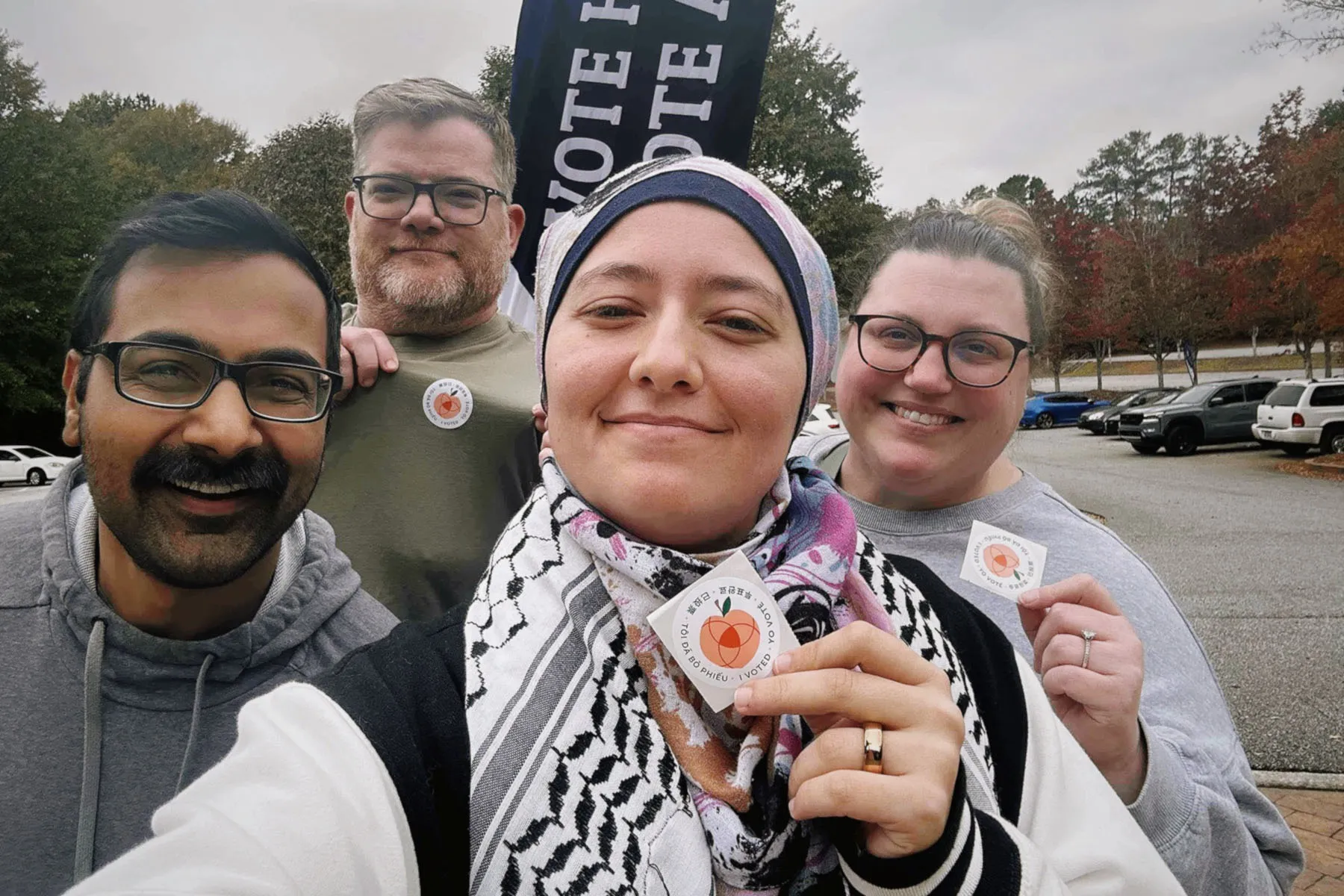 Ruwa Romman holds up an "I Voted" sticker in a selfie with her husband and their neighbors.