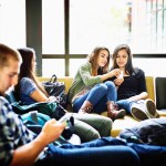 Several high school students sit around looking at their cell phones.