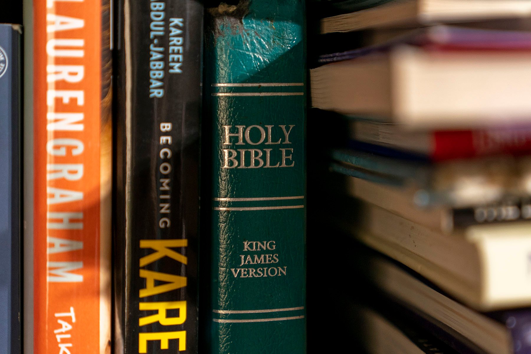 A Bible sits on a bookshelf among other books.