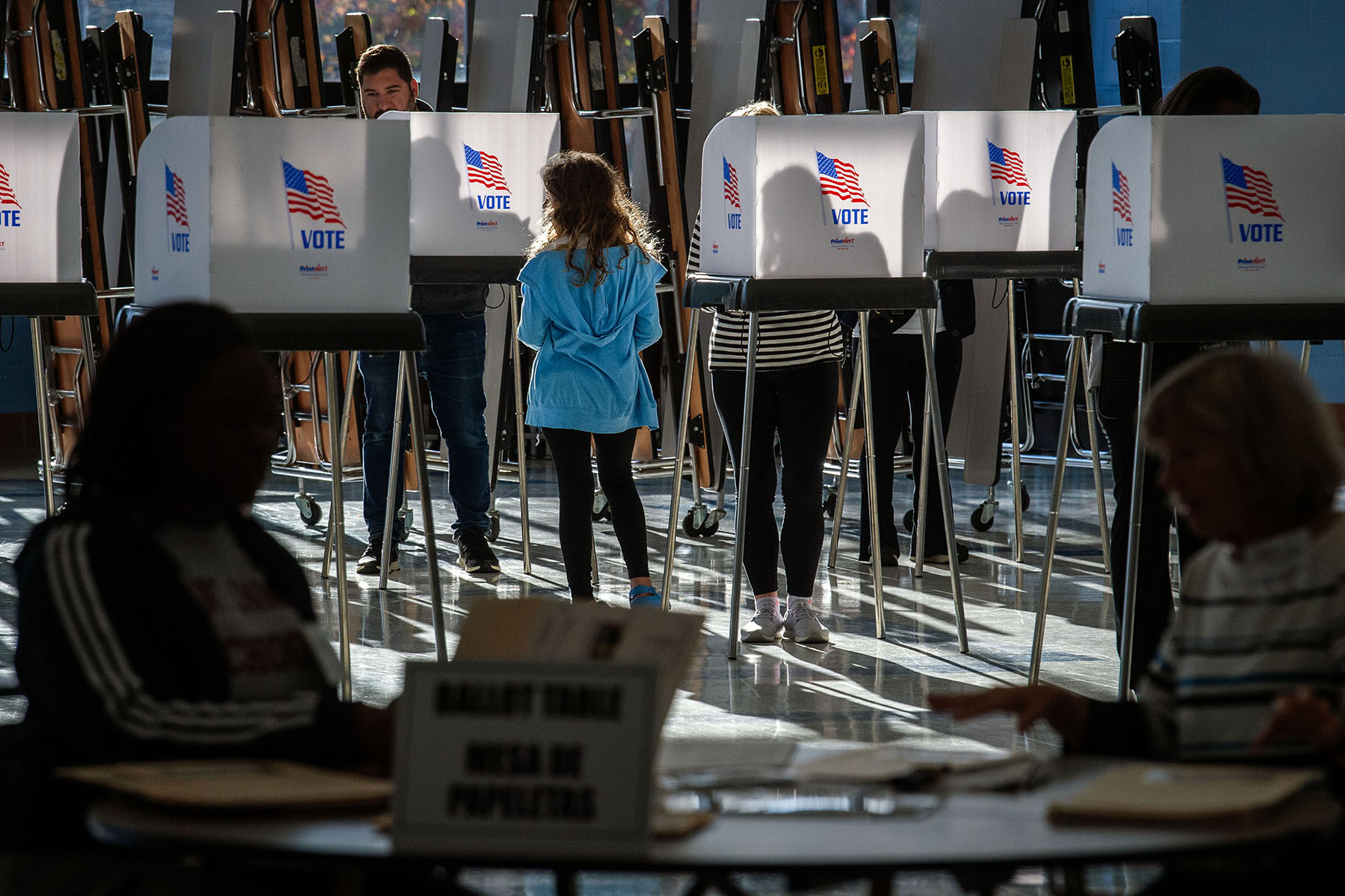 Voters silhouetted by early morning sunlight at a polling station. in the middle of the images, a little girl stands at a booth.