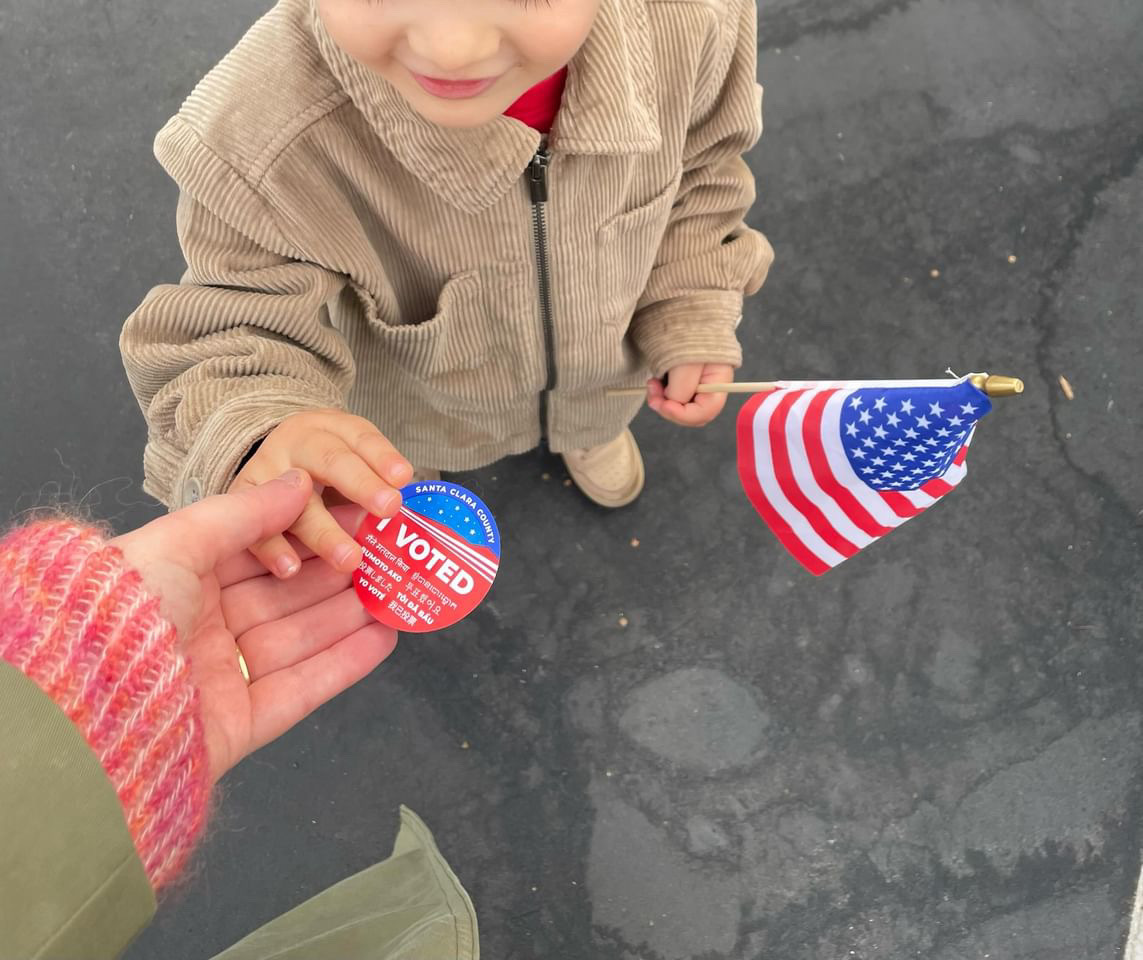 Deanna Jhaveri holds her her 3-year-old son's hand as she hands him an "I Voted" sticker. Her son holds an American flag.