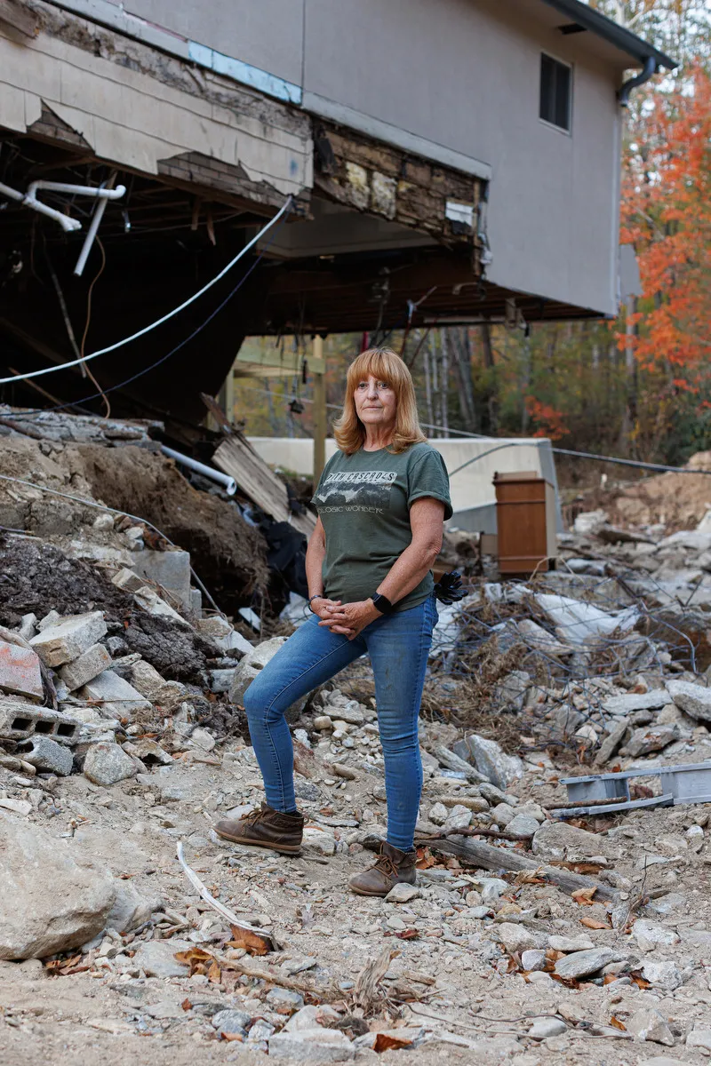 A woman stands outside amid rubble from a destroyed home.