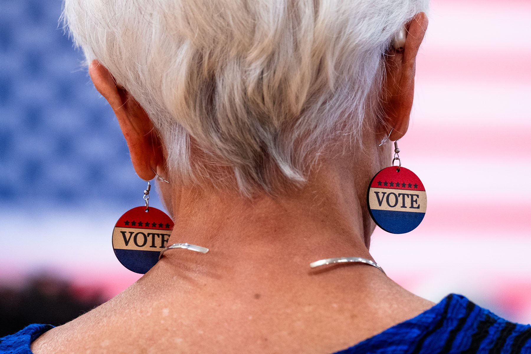 A woman, seen from the back, wears earrings that read "vote."