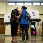 Two older women speak in front of voting booths at a polling location in Beltsville, Maryland.