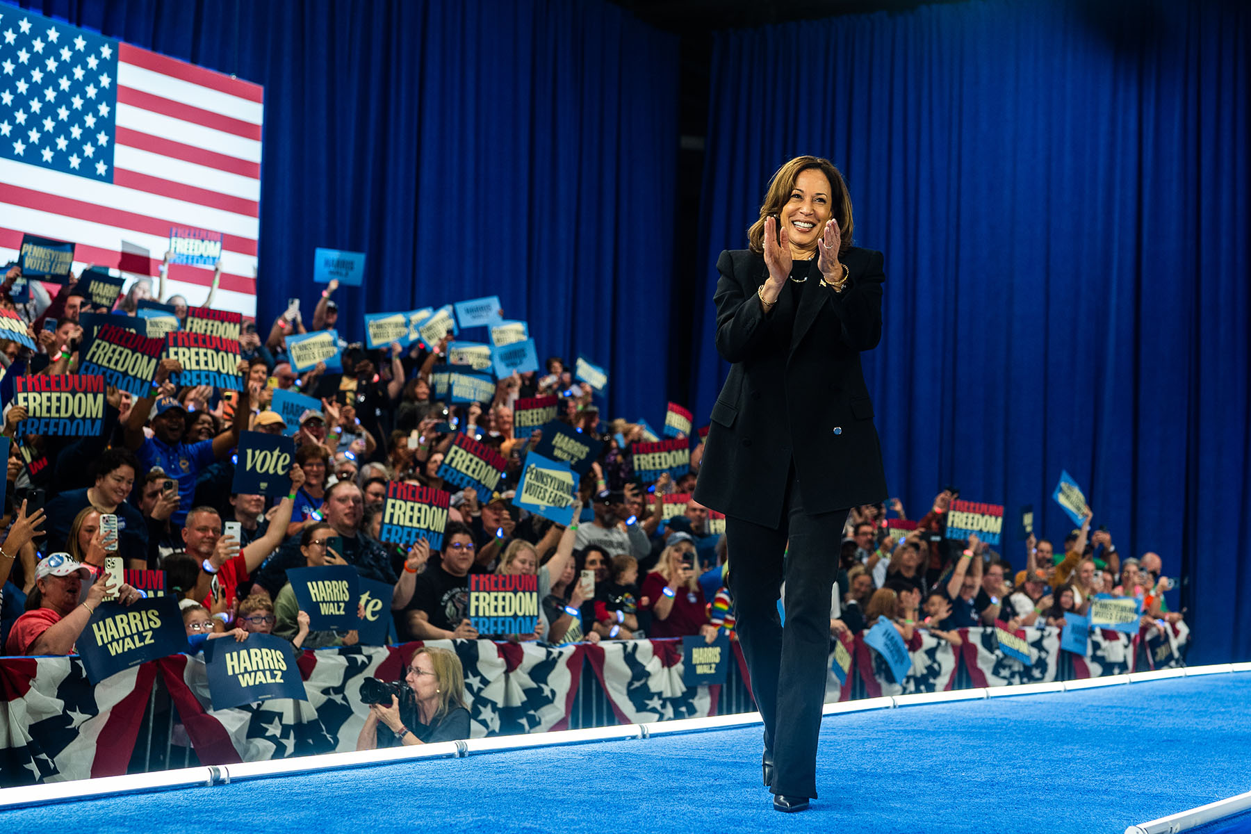 Vice President Kamala Harris takes the stage during a campaign rally at in Harrisburg, Pennsylvania. Behind her, the crowd hold up signs that read "Freedom," "Harris Walz" and "Vote"