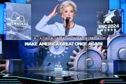 Linda McMahon speaks on stage in front of a screen with gears that says 