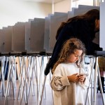 A little girl plays on a phone as her mom votes behind her at a polling place in Lake Forest, California.