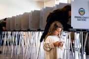 A little girl plays on a phone as her mom votes behind her at a polling place in Lake Forest, California.