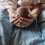 Macro view of mothers hands holding newborn boy's head