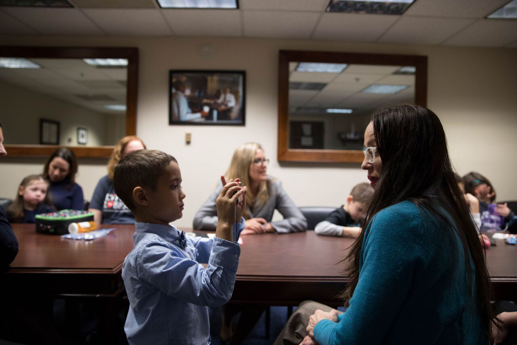 A young boy, Aire Watkins, holds up a phone to take a picture of his mother, Val Watkins, while Rep. Jennifer Wexton listens in the background during a 2019 Little Lobbyists meeting.