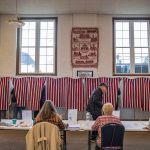 A voter passes by a table of four seated female poll workers.