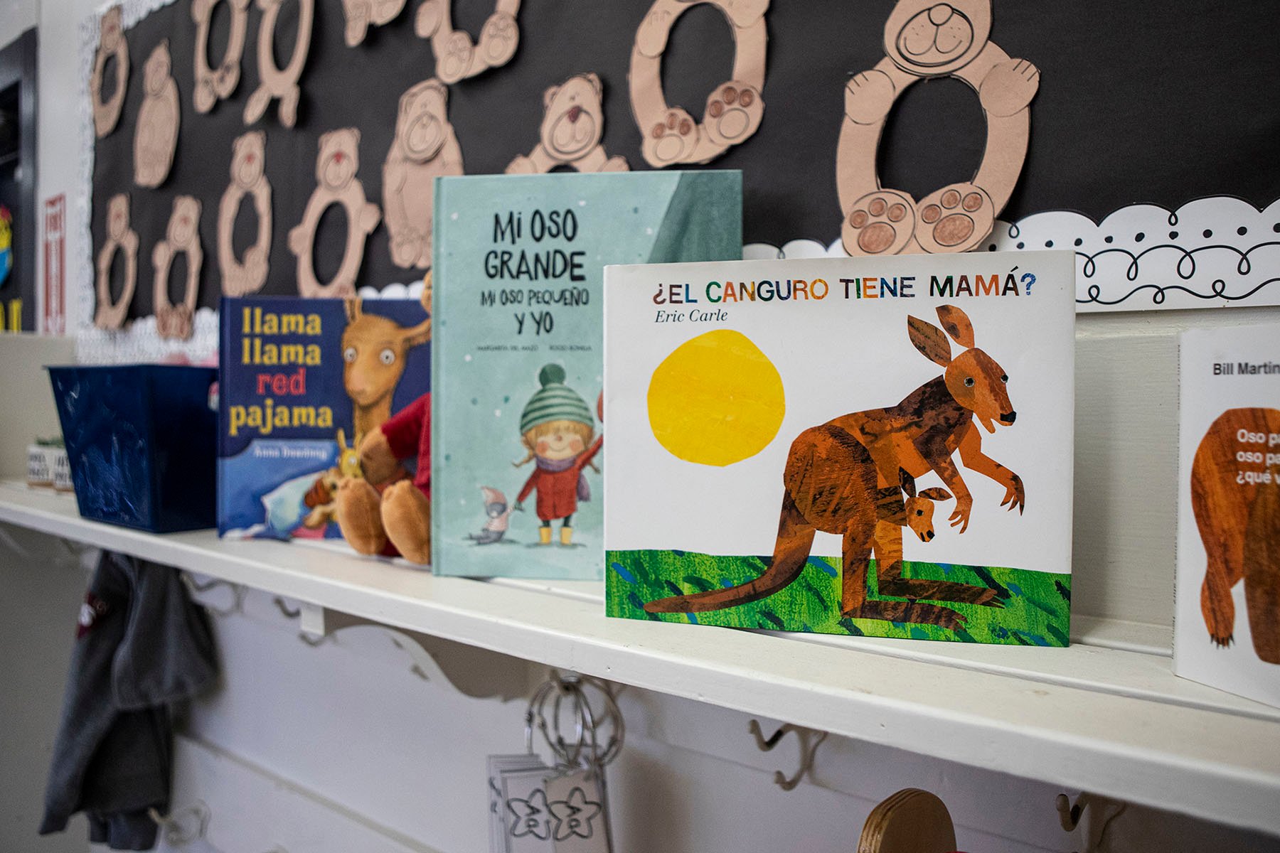 A row of children's books in Spanish and English lined up on a shelf on the classroom wall.