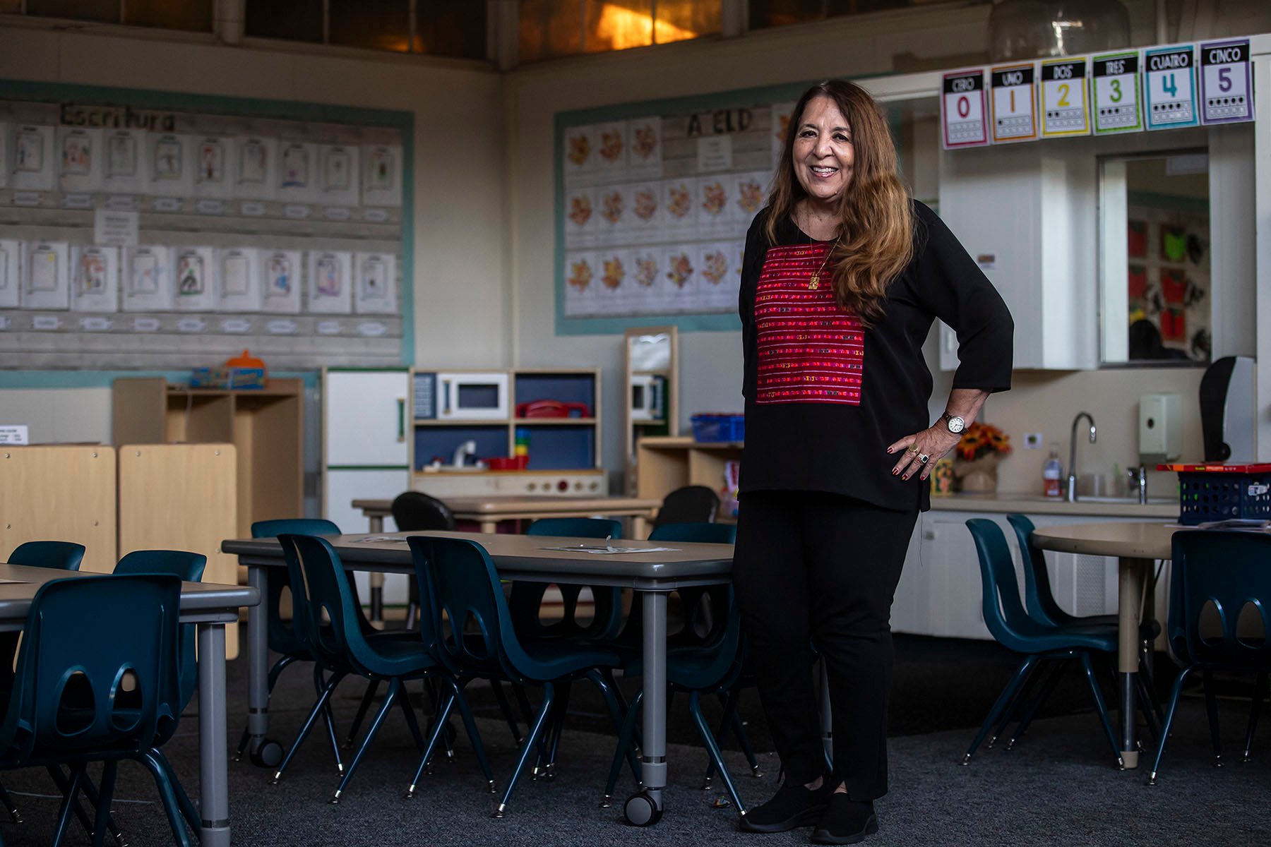 A person stands with her hand on her hip in the middle of a kindergarten classroom.