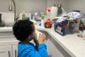 A young boy watches a cartoon on a cell phone in a kitchen.