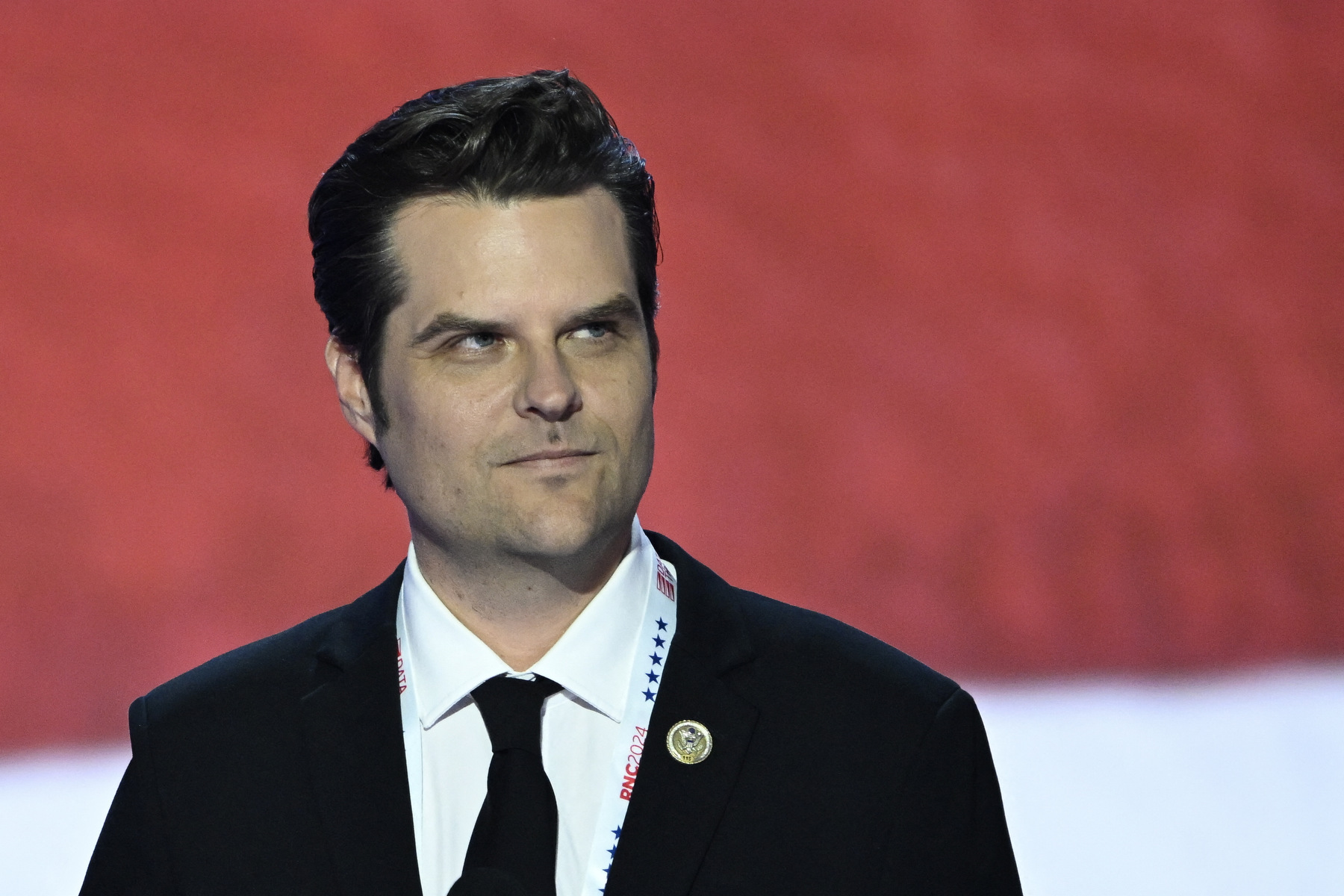 A closeup portrait of Matt Gaetz against a red backdrop.