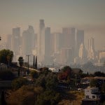 The Los Angeles skyline is shrouded in smog with houses on a hill in the foreground.