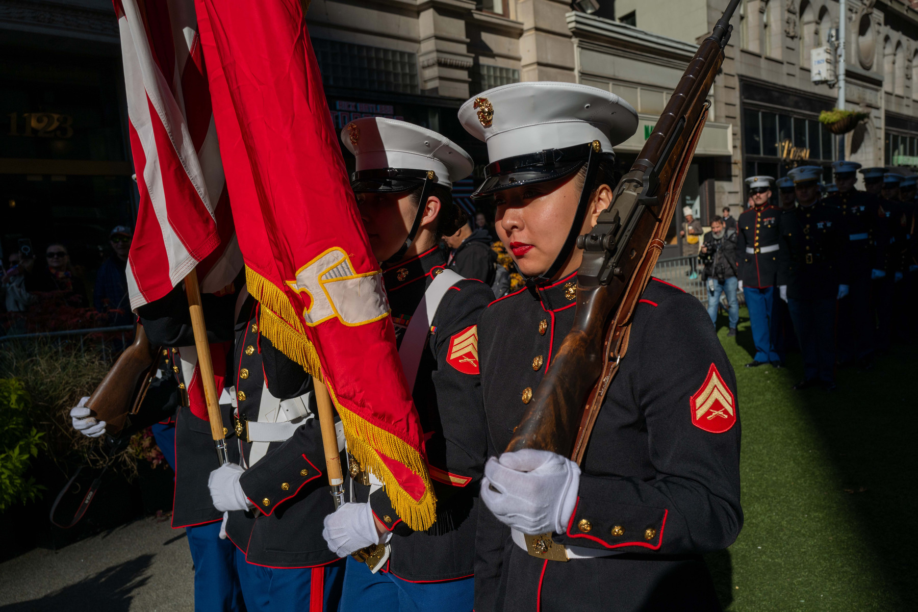 A line of Marines carry flags and guns in a parade.