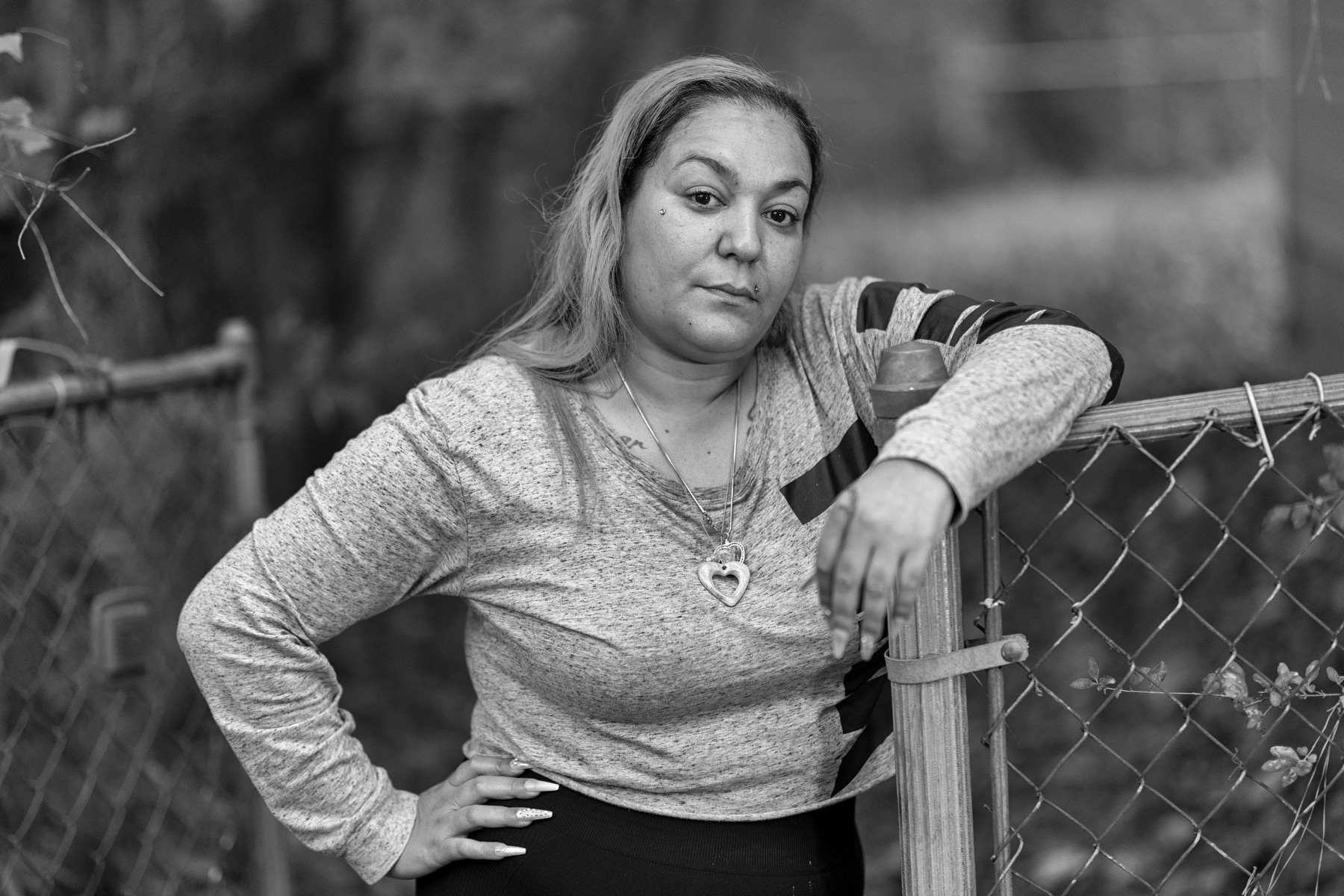 A woman leans on a fence while looking into the camera.