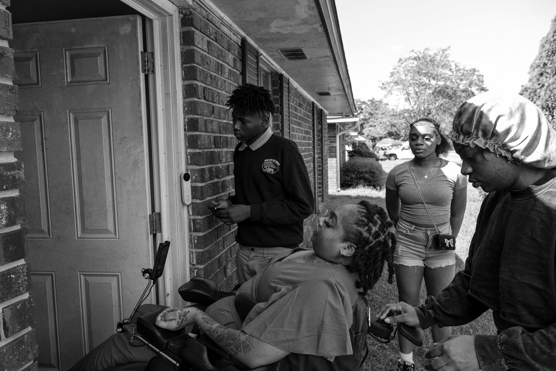 A woman using a wheelchair is pushed into a home, surrounded by friends and family.