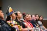 A group of Indigenous women sit in a line, listening to an unseen speaker.