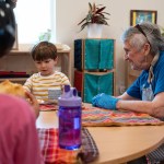 A resident at Wesley Homes and children from Bezos Academy are seen having lunch together.