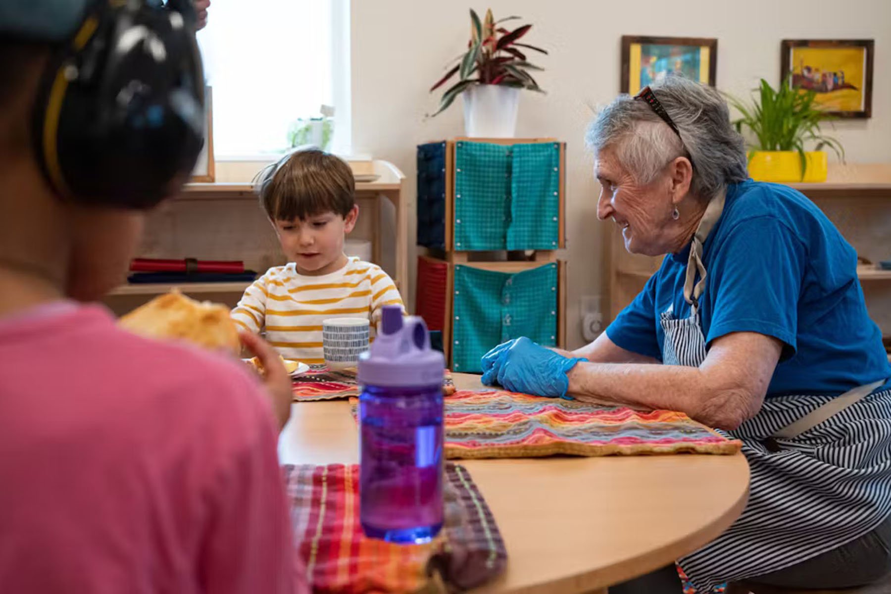 A resident at Wesley Homes and children from Bezos Academy are seen having lunch together.