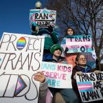 Protestors hold up trans pride signs.