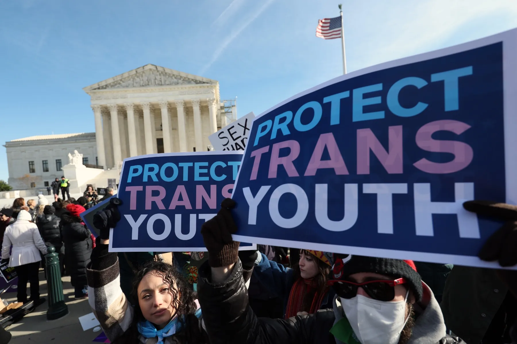 Protesters hold signs in front of the Supreme Court that read "Protect Trans Youth"