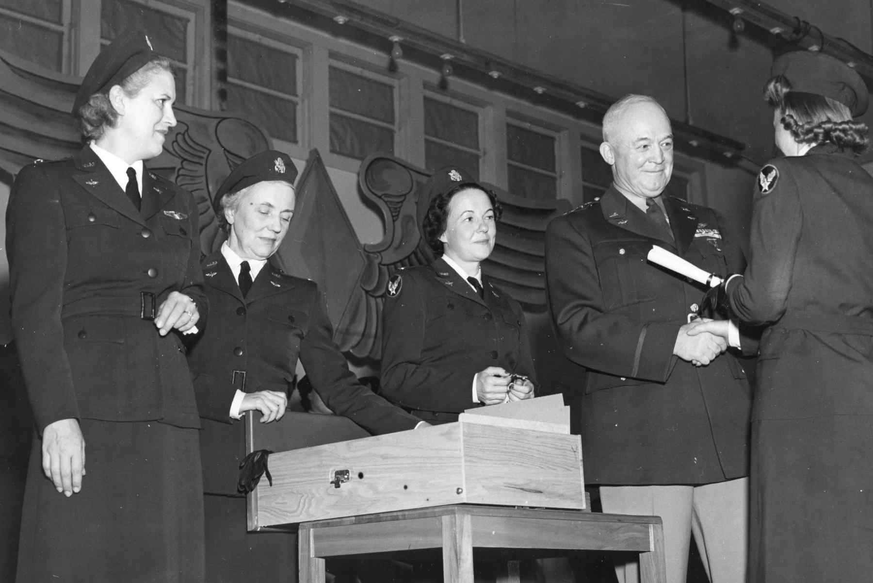 Three Women's Airforce Service Pilots (WASPs) watch Gen. Henry Arnold hand a diploma to another WASP who just graduated from the last training class.