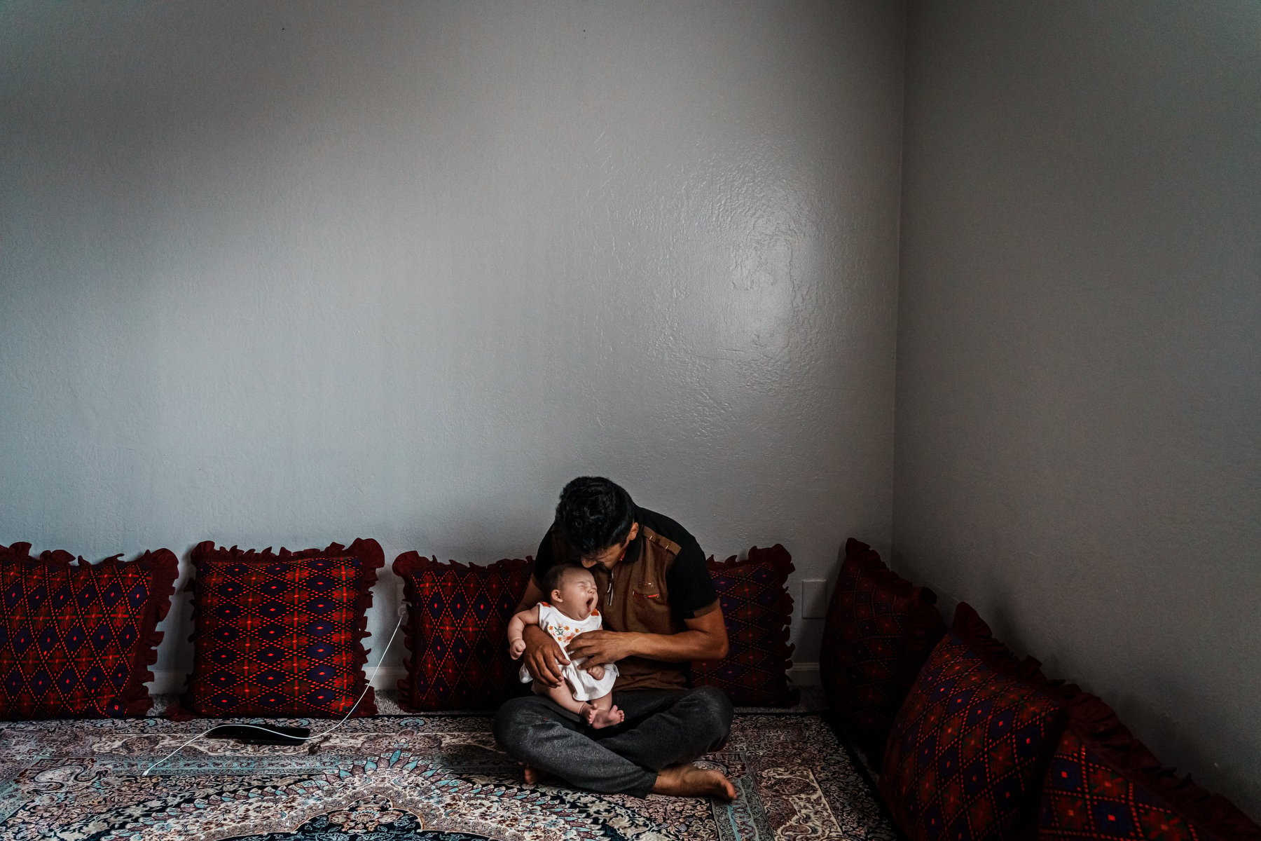 A father holds his newborn baby in his lap while seated on the floor.