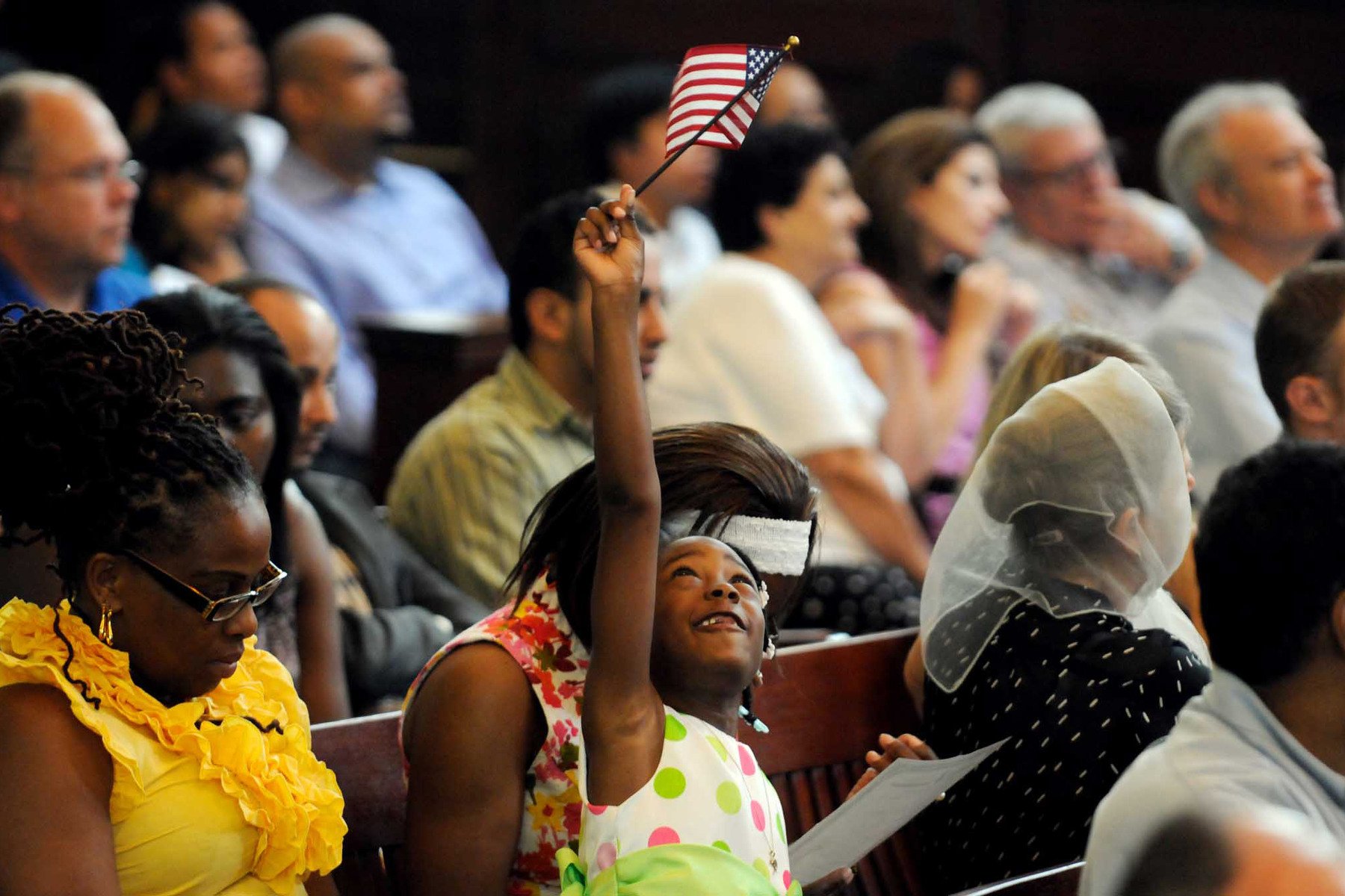 A child waves an American flag while seated in a room full of people.