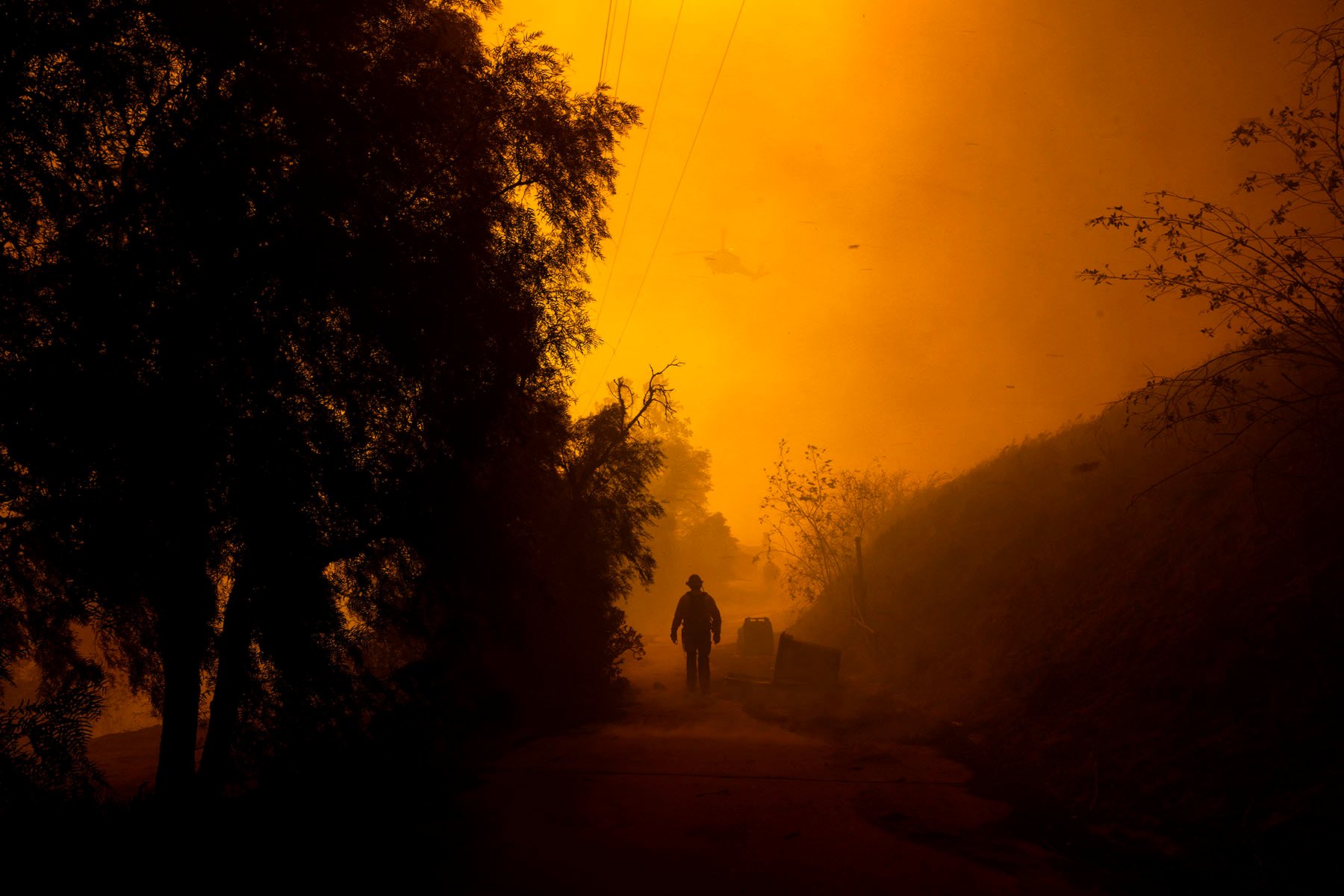 A firefighter walks on a path engulfed in smoke and embers as high winds push the Mountain Fire in Camarillo Heights, Camarillo, California.