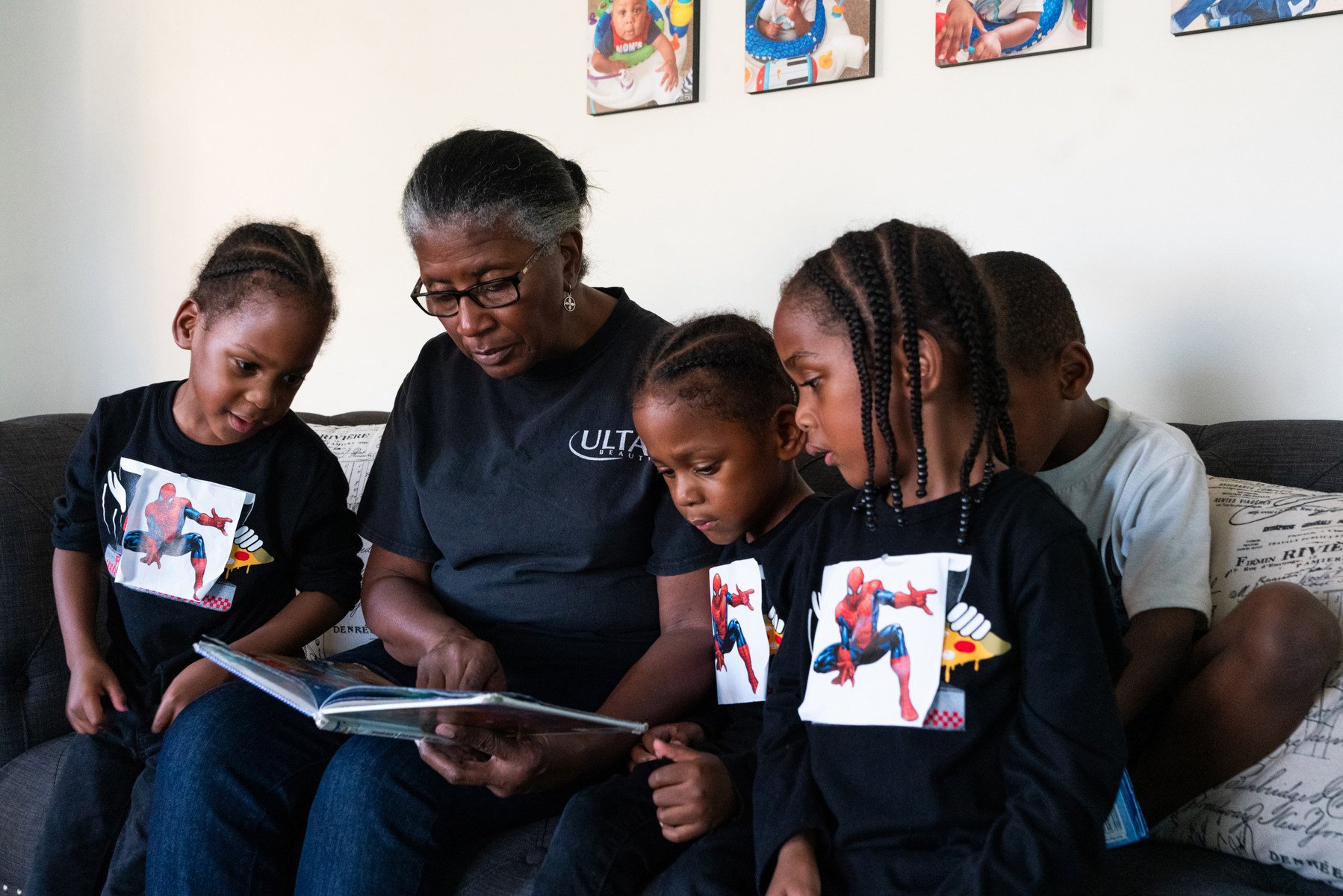 Four children sit on a sofa listening to a woman reading them a book.