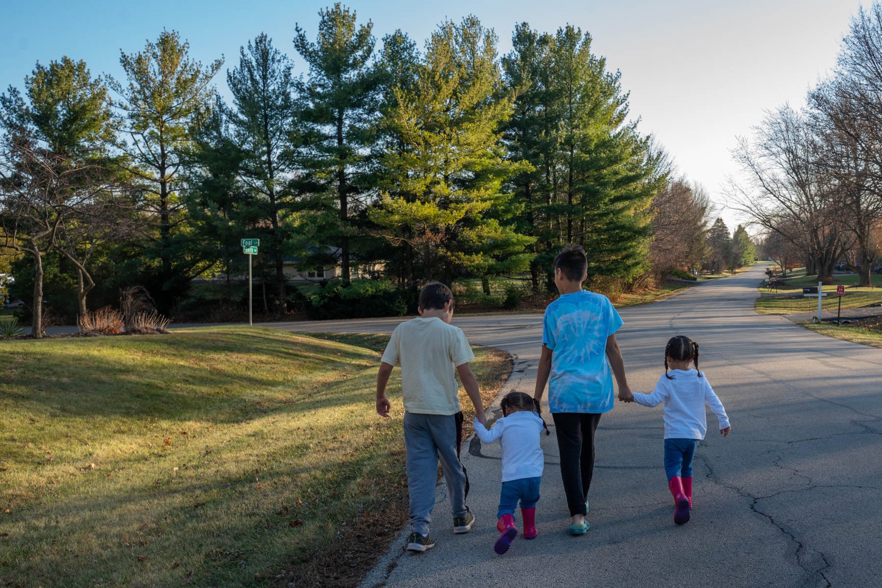 Four children walk down a street, all holding hands.