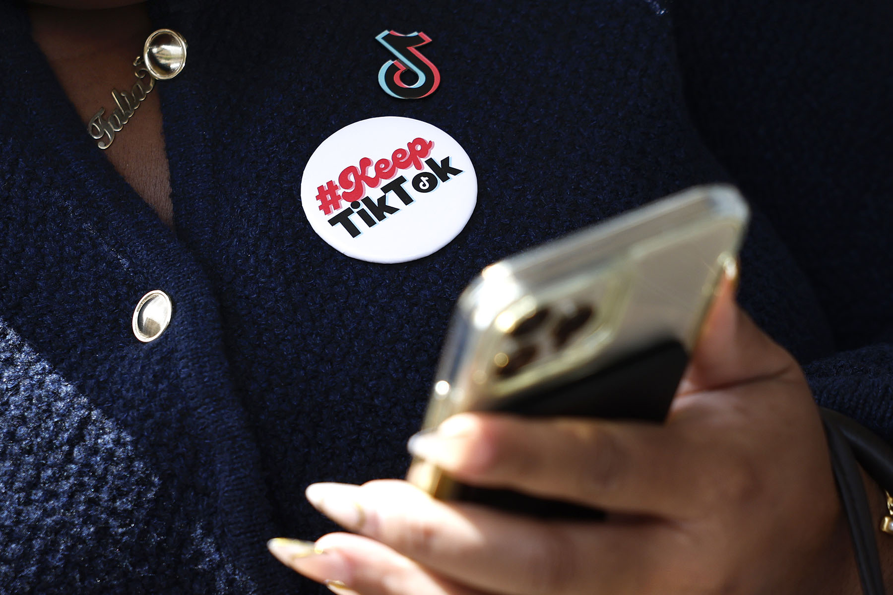 A woman wears a "#KeepTikTok" pin as she uses her phone.