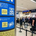 A TSA sign with limits on liquids is seen with a passenger security line in the background