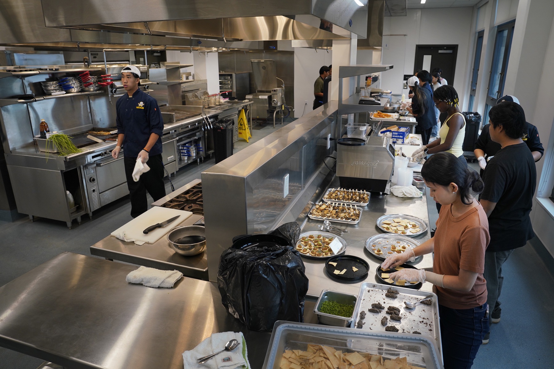 Students work in a kitchen preparing pupus.