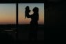 A silhouette of a person holding a child near a window.