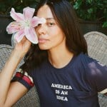 Aurora James poses while holding a flower and wearing a shirt that reads 