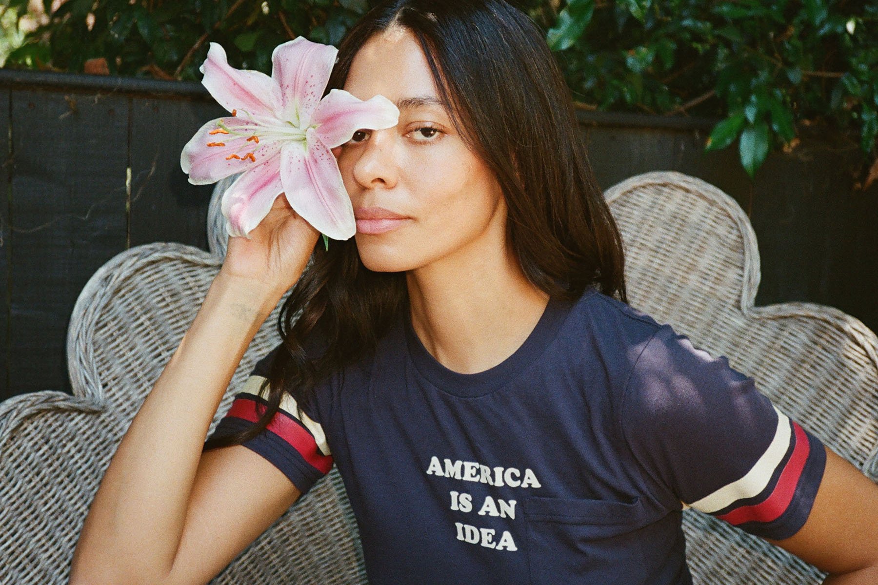 Aurora James poses while holding a flower and wearing a shirt that reads "American is an idea."